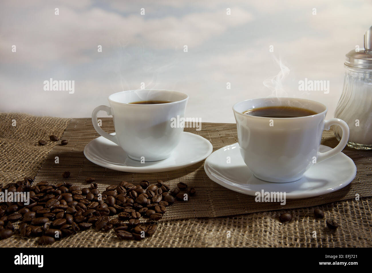 Two cups of steaming coffee, coffee beans in front Stock Photo