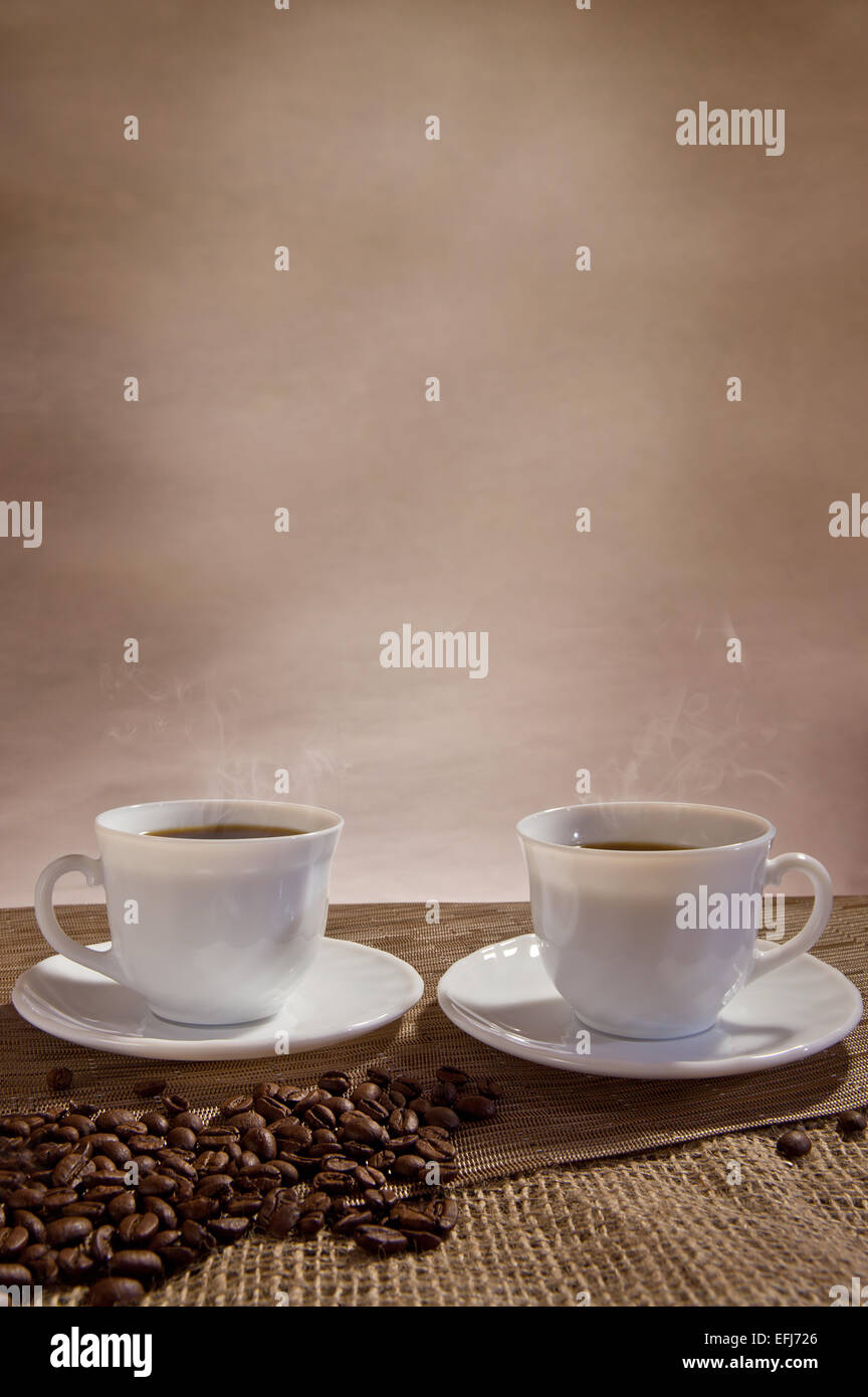 Two cups of steaming coffee, coffee beans in front Stock Photo