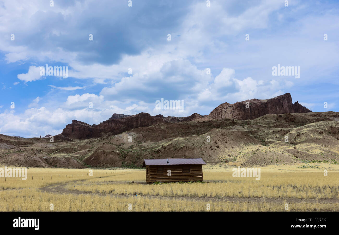 Isolated Log Cabin Flanked By High Rocky Mountains And Grassland