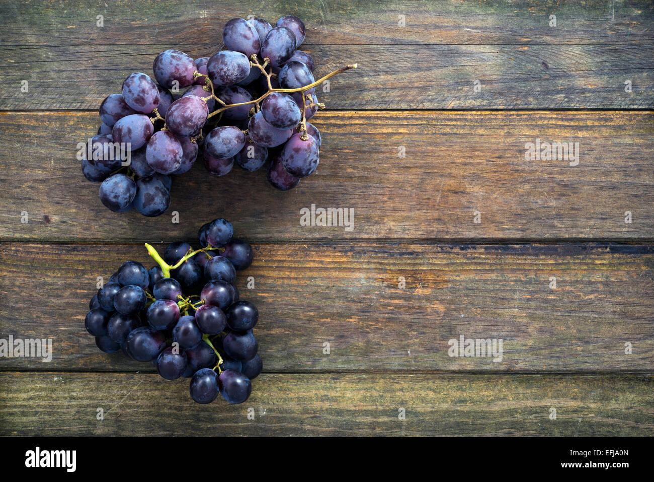two bunches of black grapes on an old wooden table. Space for text Stock Photo