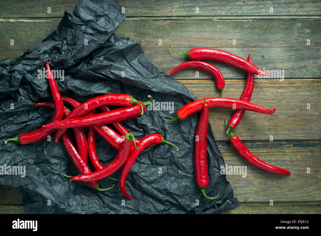 Chilli peppers on a black paper on an old wooden table Stock Photo