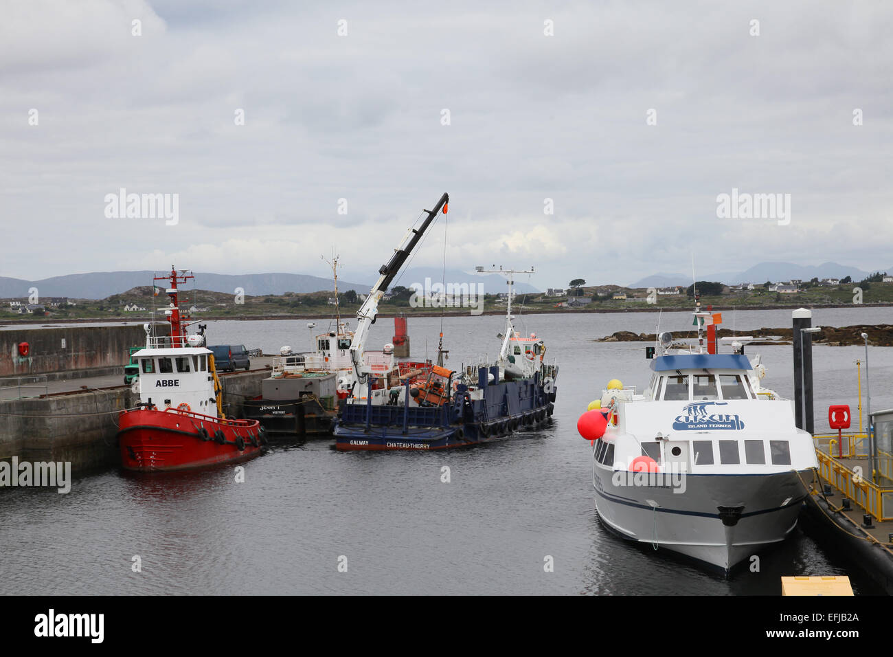 Ferry awaitng to leave for the Aran Isles fron Rossaveal with a fishing boat moored the jetty and a coaster being loaded. Stock Photo