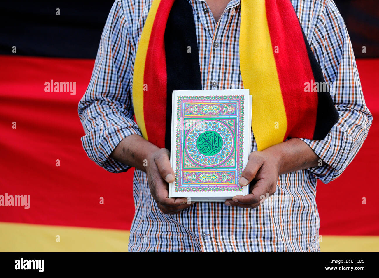 Turkish man wearing scarf in German flags colors (black red gold) keeps the Koran, the holy book of the Muslims in his hands. Dortmund/Germany Stock Photo
