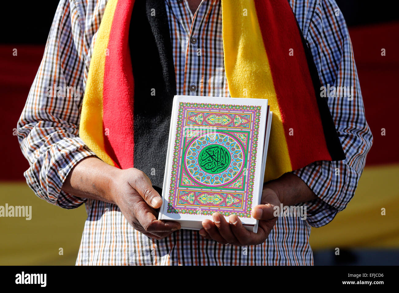 Turkish man wearing scarf in German flags colors (black red gold) keeps the Koran, the holy book of the Muslims in his hands. Dortmund/Germany Stock Photo