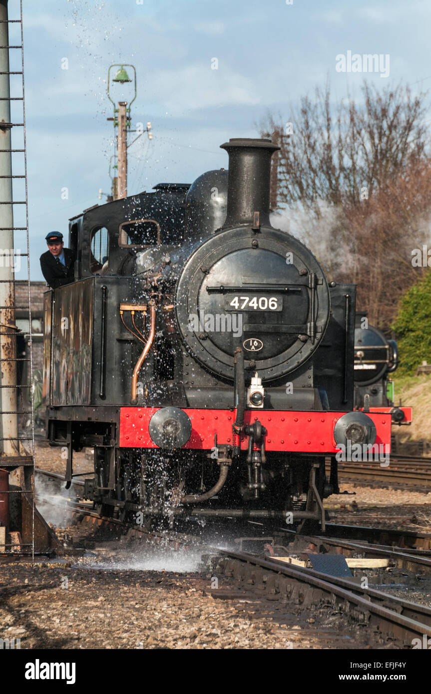 Jinty Class 3F 0-6-0T steam loco under an overflowing water tower to take on water at Loughborough on the Great Central Railway Stock Photo