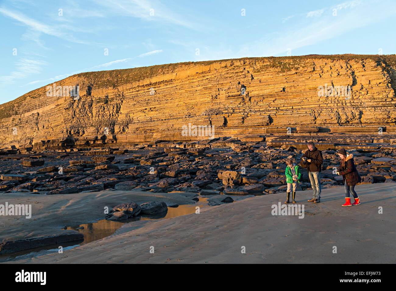 Man with children on beach with sea cliffs, Southerndown, Wales, UK Stock Photo