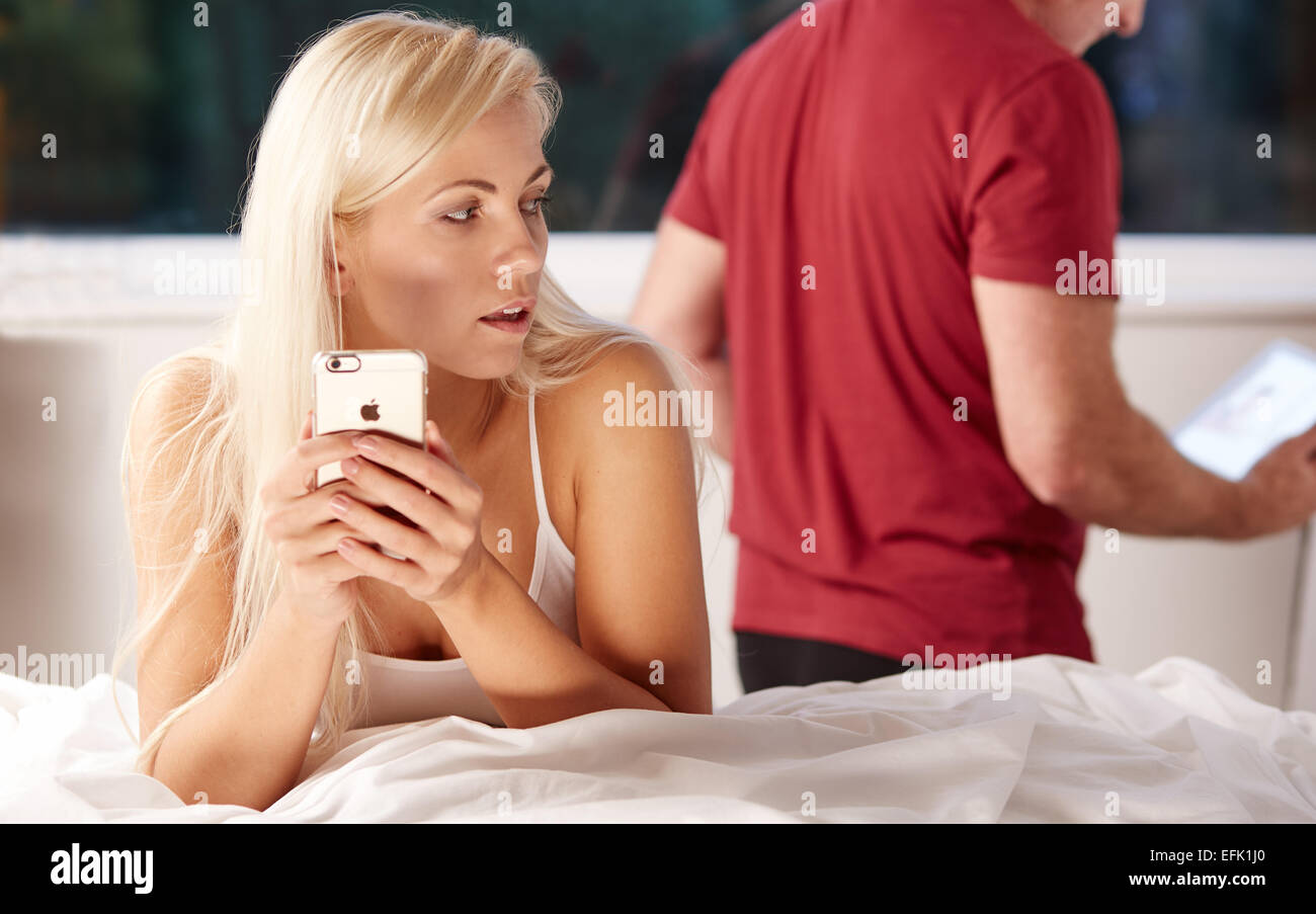 Woman looking sneakily at messages on her phone whilst partners back is turned Stock Photo