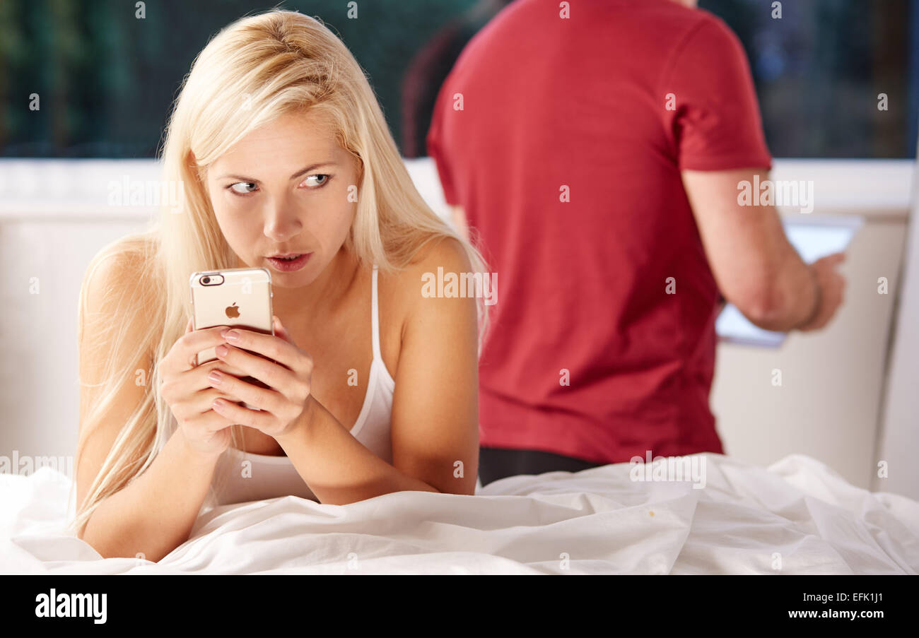 Woman looking sneakily at messages on her phone whilst partners back is turned Stock Photo