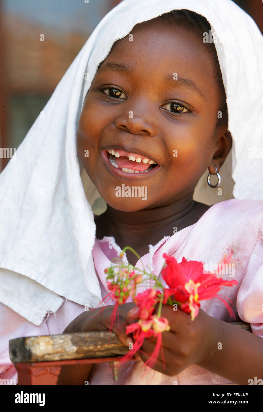 Kenya, five year old girl wearing a veil and holding hibiscus flower in
