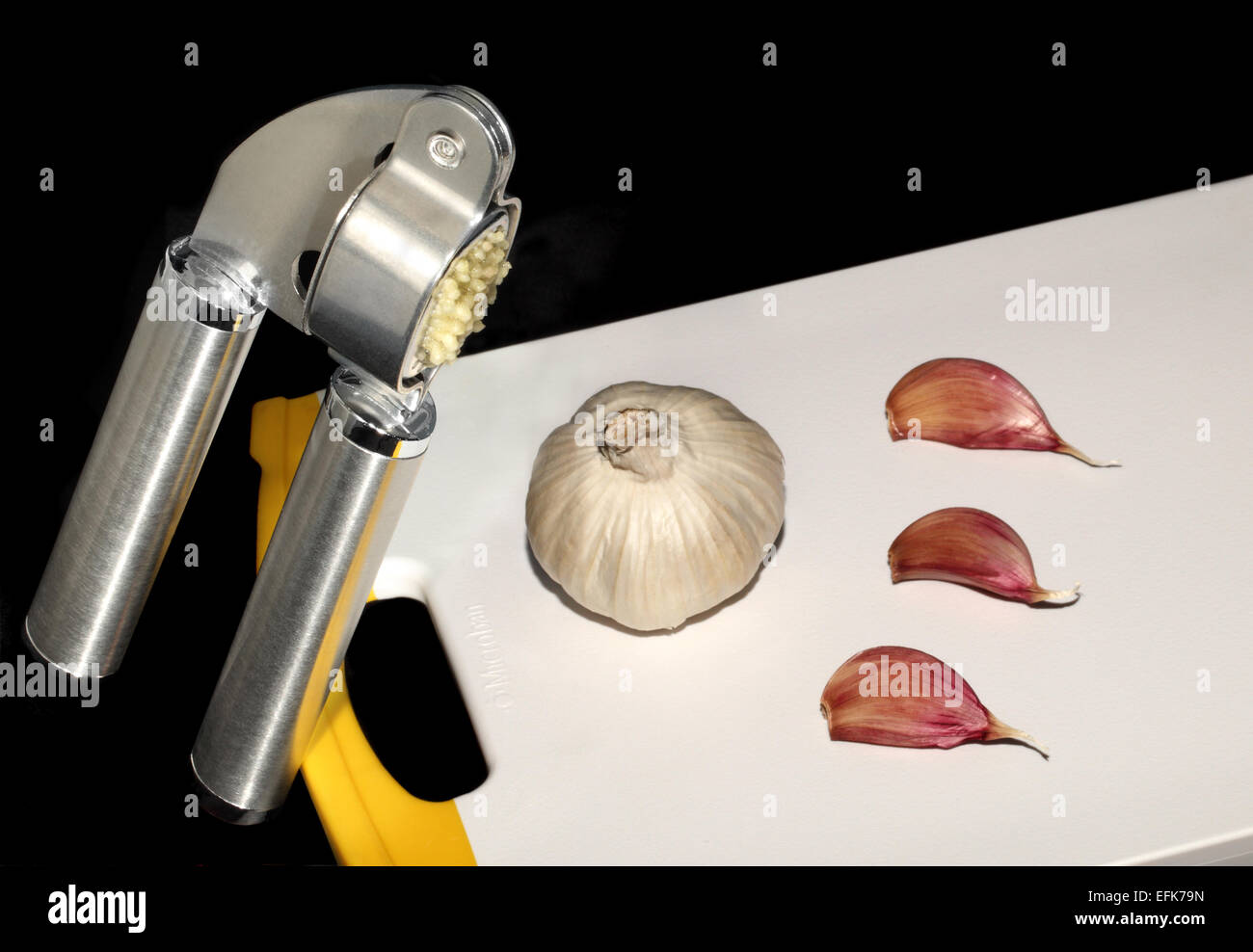 Garlic being 'pressed' in a garlic press or crusher, with a garlic bulb