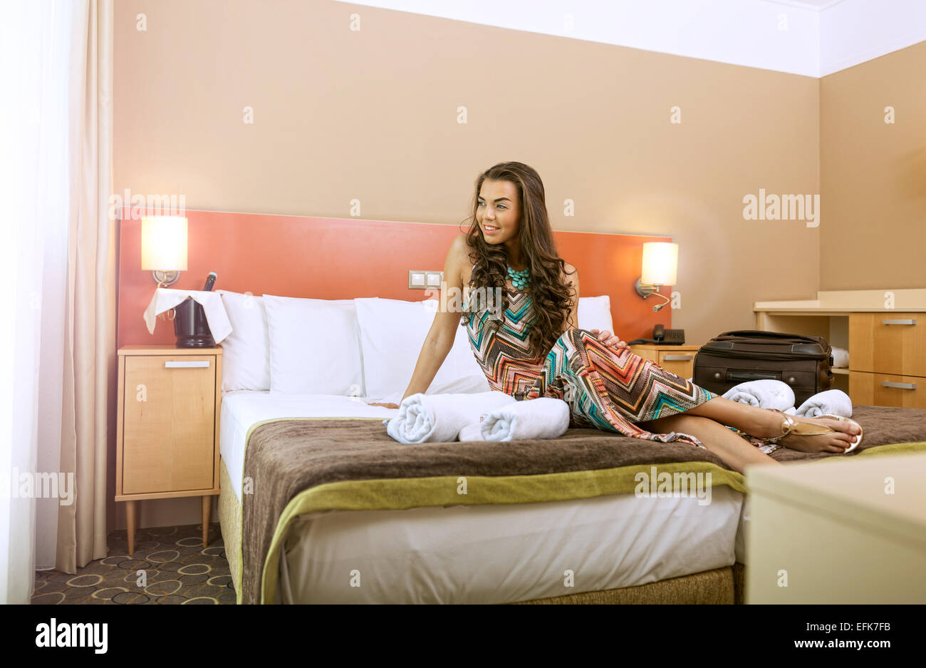 Young woman sitting in the bed of a hotel room Stock Photo