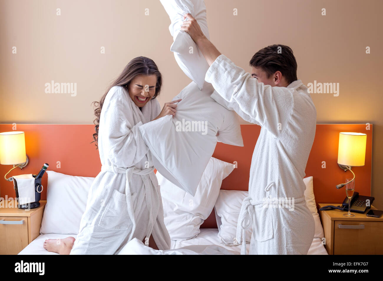 Happy Couple Having Pillow Fight in Hotel Room Stock Photo
