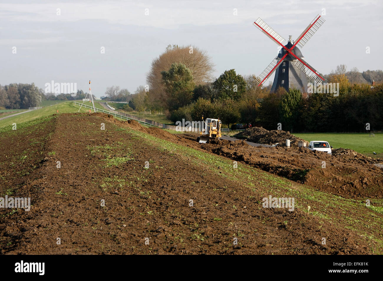 The dike is built 1.50 m higher in Aschwarden. In front of the dike at the wind mill in Aschwarden roll trucks, trailers, excavators and other technology to secure the dike between the Weser island Harriersand and the land beyond. Photo: Klaus Nowottnick D Stock Photo
