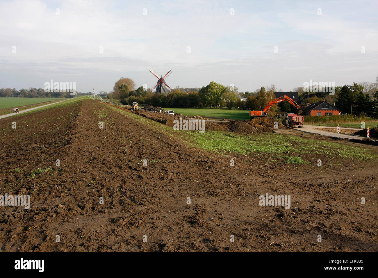 The dike is built 1.50 m higher in Aschwarden. In front of the dike at the wind mill in Aschwarden roll trucks, trailers, excavators and other technology to secure the dike between the Weser island Harriersand and the land beyond. Photo: Klaus Nowottnick D Stock Photo