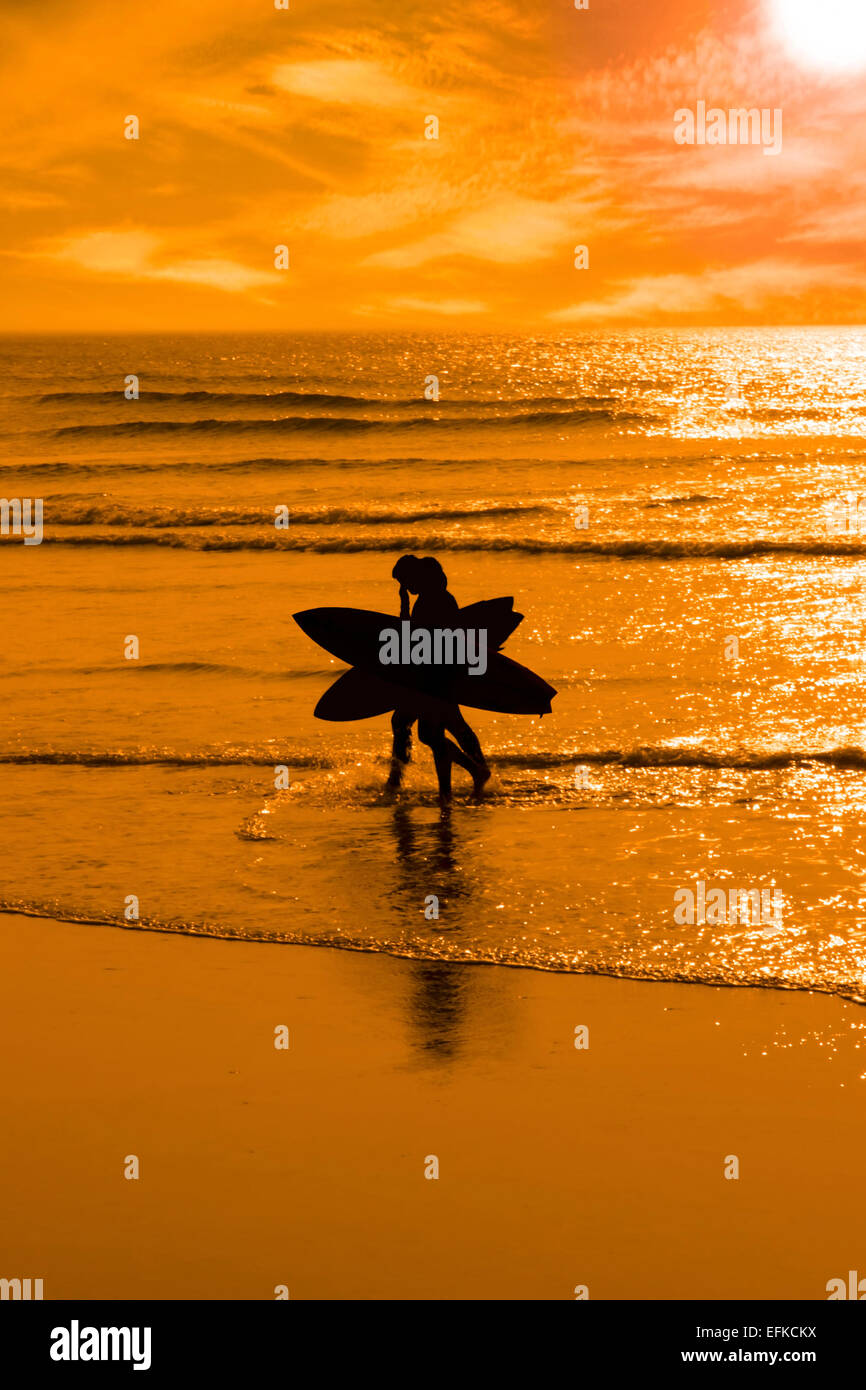 silhouette of surfing couple walking from the sea to the beach just before sunset with silhouette in shape of an angel or x Stock Photo