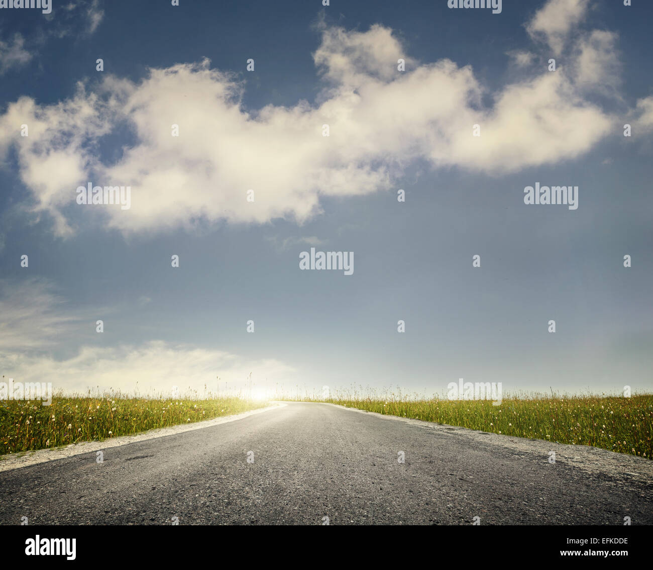 Wide road and green meadow at blue cloudy sky background Stock Photo