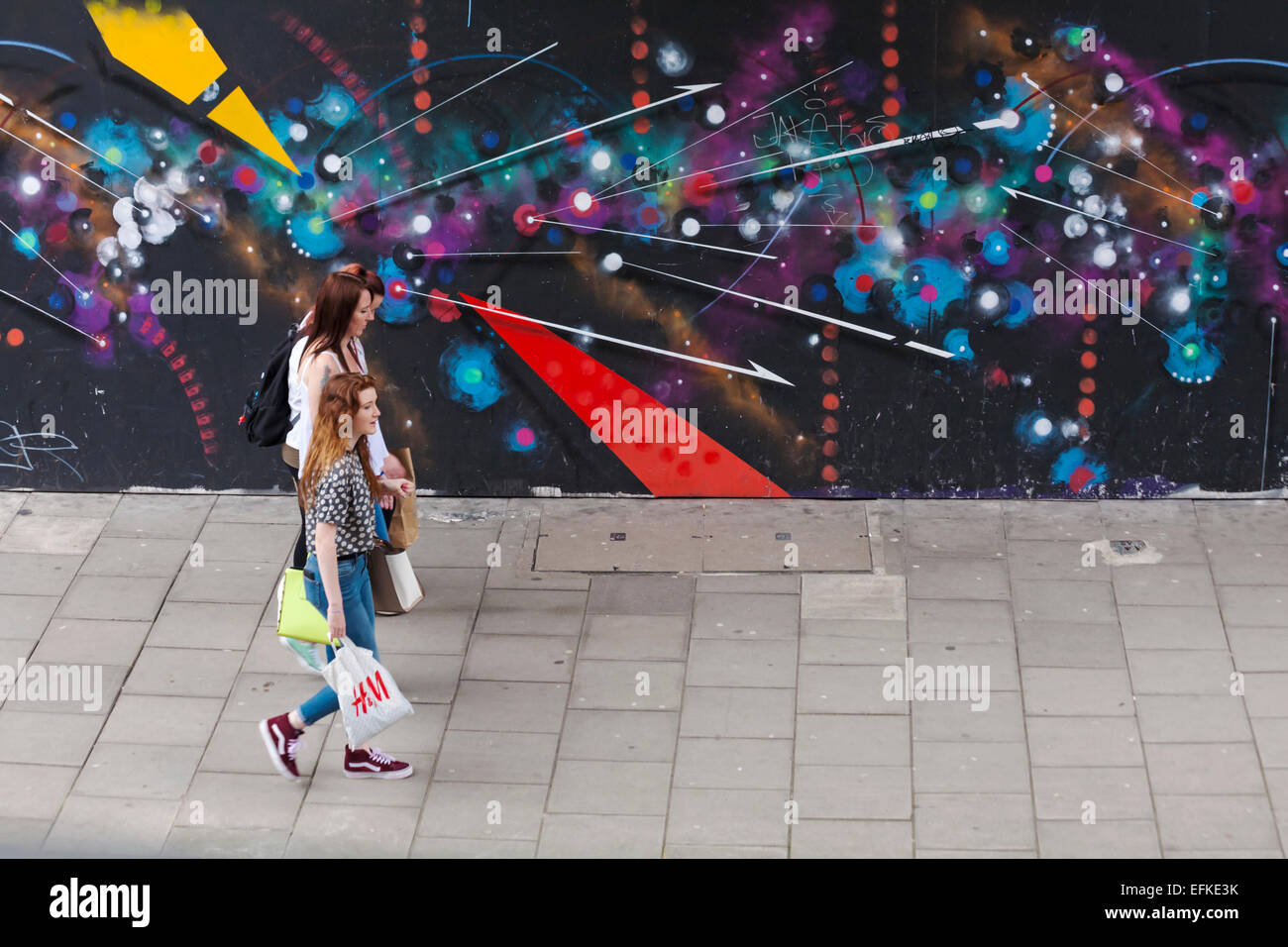 Three young women walking past street art graffiti at Bristol Stock Photo