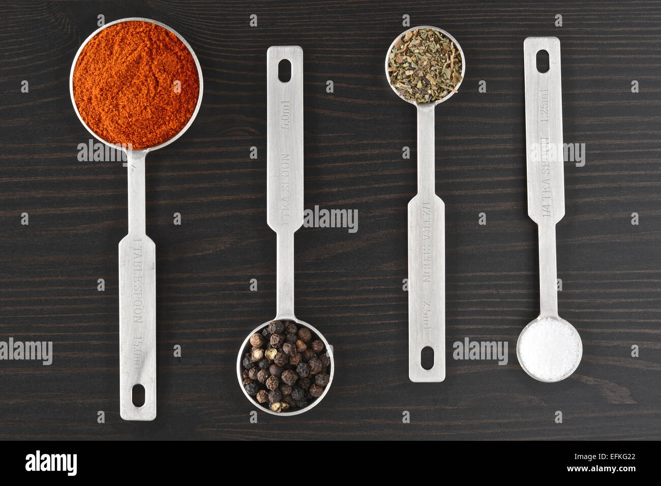 Peppercorns, Paprika, Thyme and salt in measuring spoons on a dark wooden surface Stock Photo