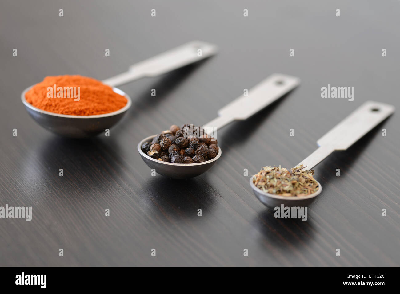 Peppercorns, Paprika and thyme in measuring spoons on a dark wooden surface Stock Photo