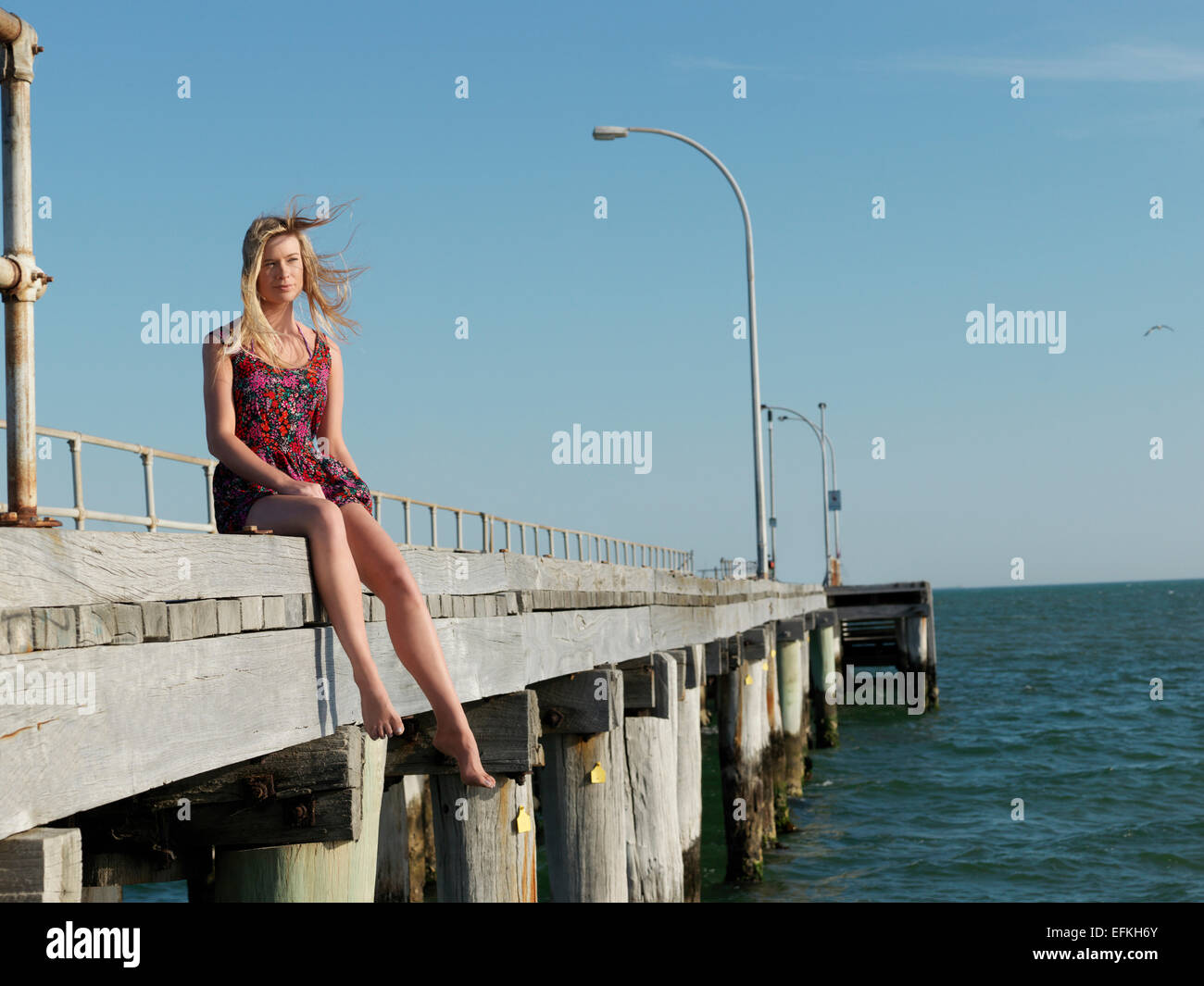 Young woman sitting on breezy pier, Altona, Melbourne, Victoria, Australia Stock Photo
