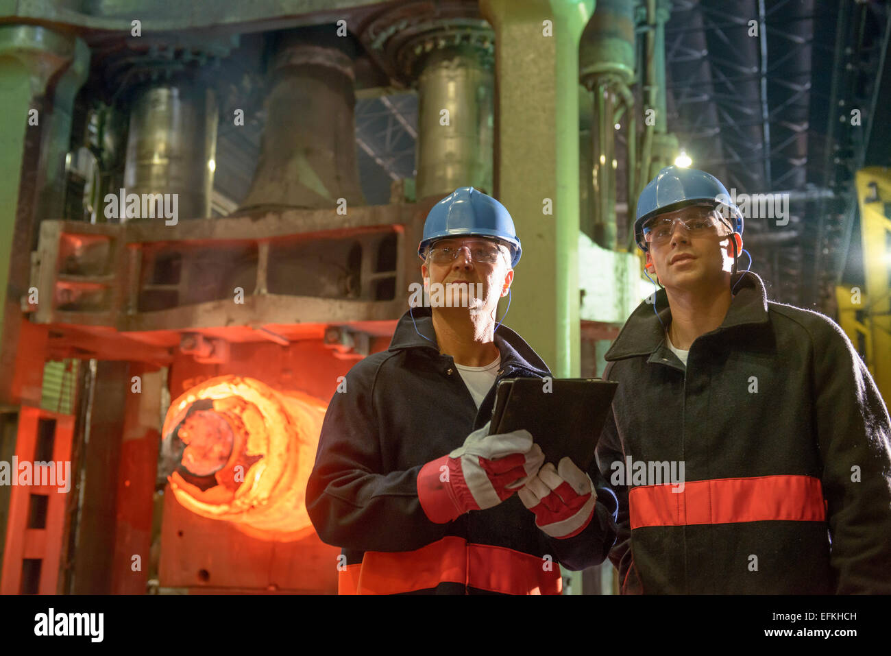 Steelworkers using digital tablet in front of 10,000 tonne forging press in steelworks Stock Photo