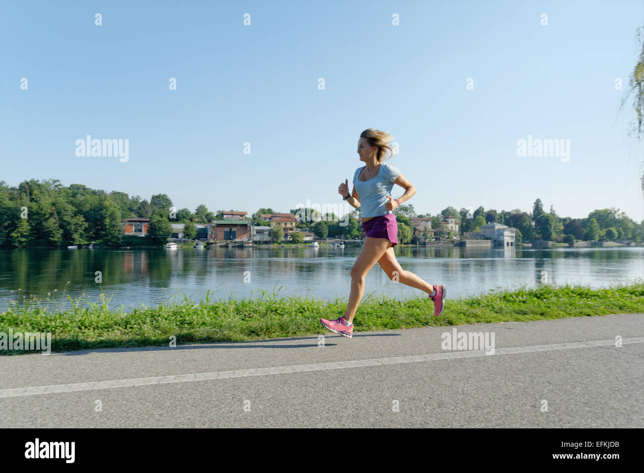 Mid adult woman running on road alongside lake Stock Photo