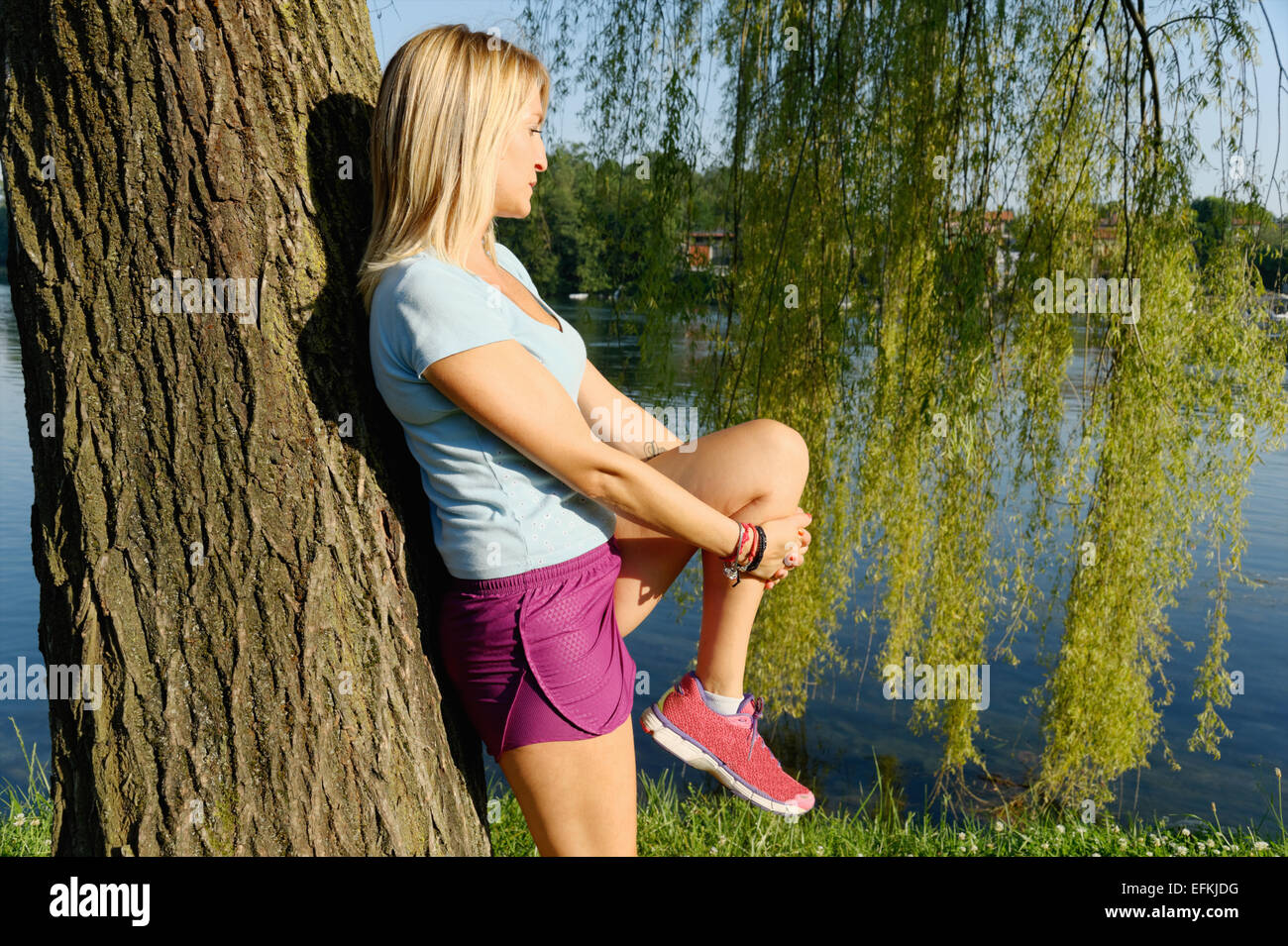 Mid adult woman stretching against tree Stock Photo