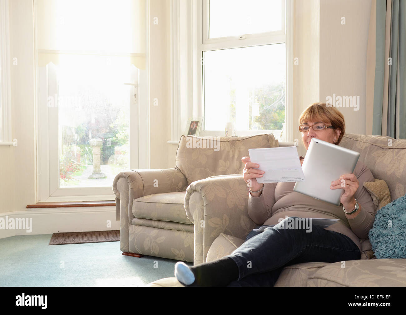 Senior woman sitting on sofa using digital tablet Stock Photo - Alamy