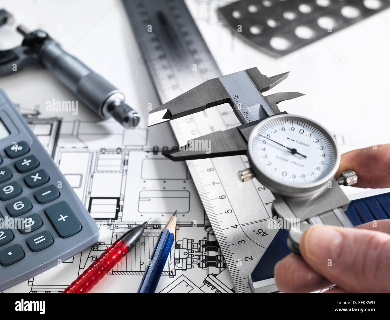Engineer holding dial caliper with measurement equipment sitting on  technical drawing Stock Photo