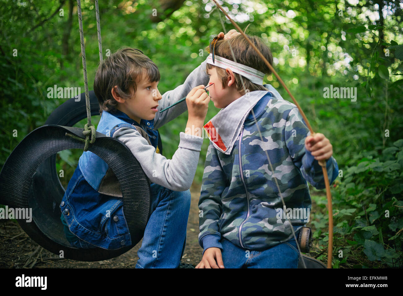 Boy face painting friend whilst playing in forest Stock Photo