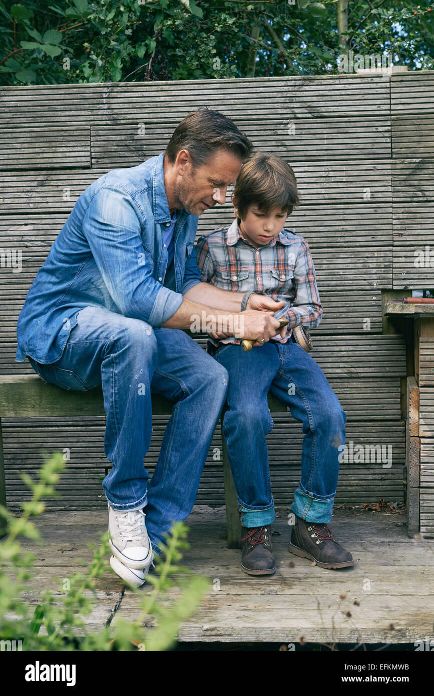 Father showing son how to use pocket knife on allotment Stock Photo