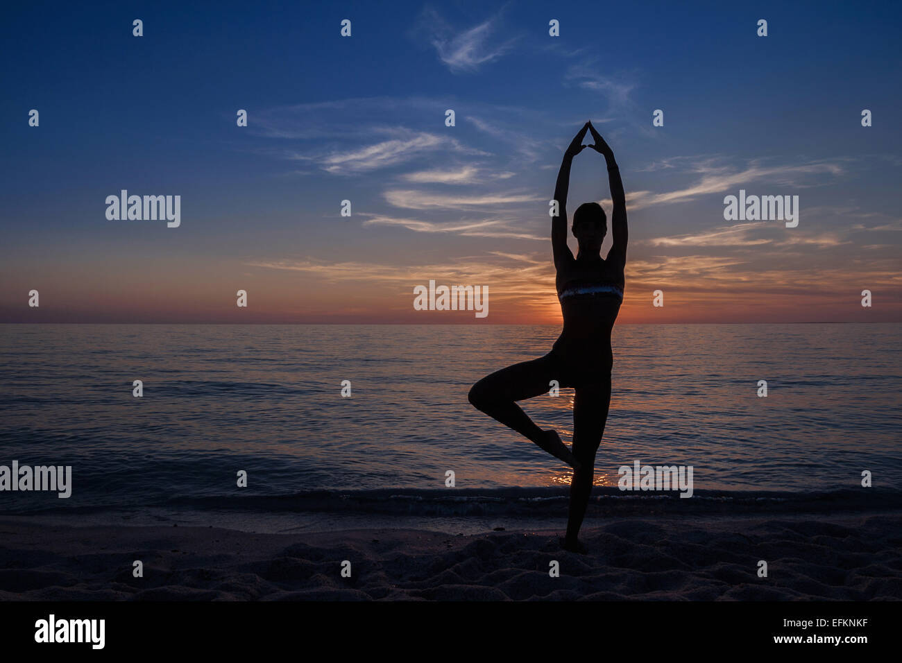 Silhouetted young woman in yoga pose on beach at sunset, Oristano ...
