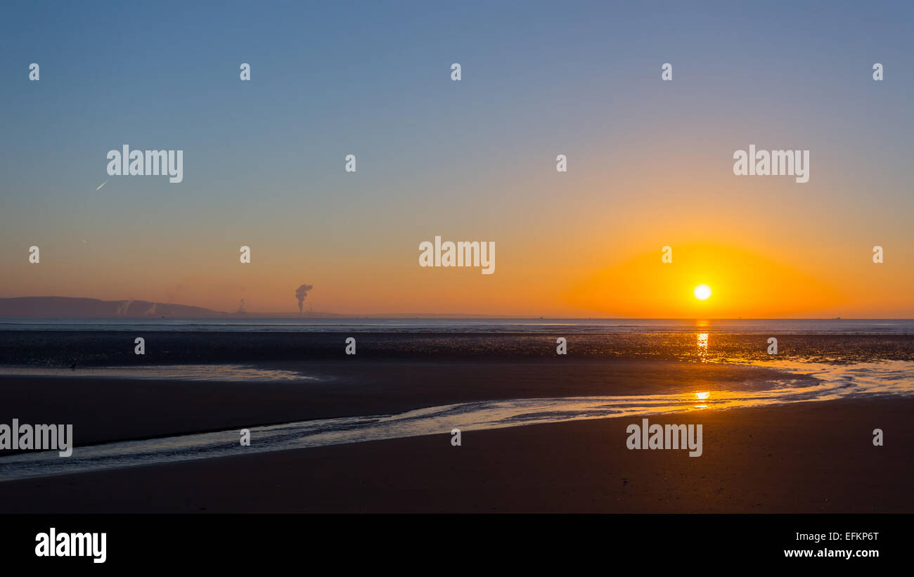 Sunrise over Swansea beach, South Wales, on a clear winter morning, with the industrial emissions from Port Talbot visible acros Stock Photo