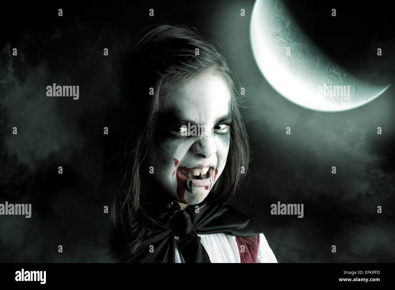 Girl with face-paint and Halloween vampire costume in a dark background with the moon Stock Photo