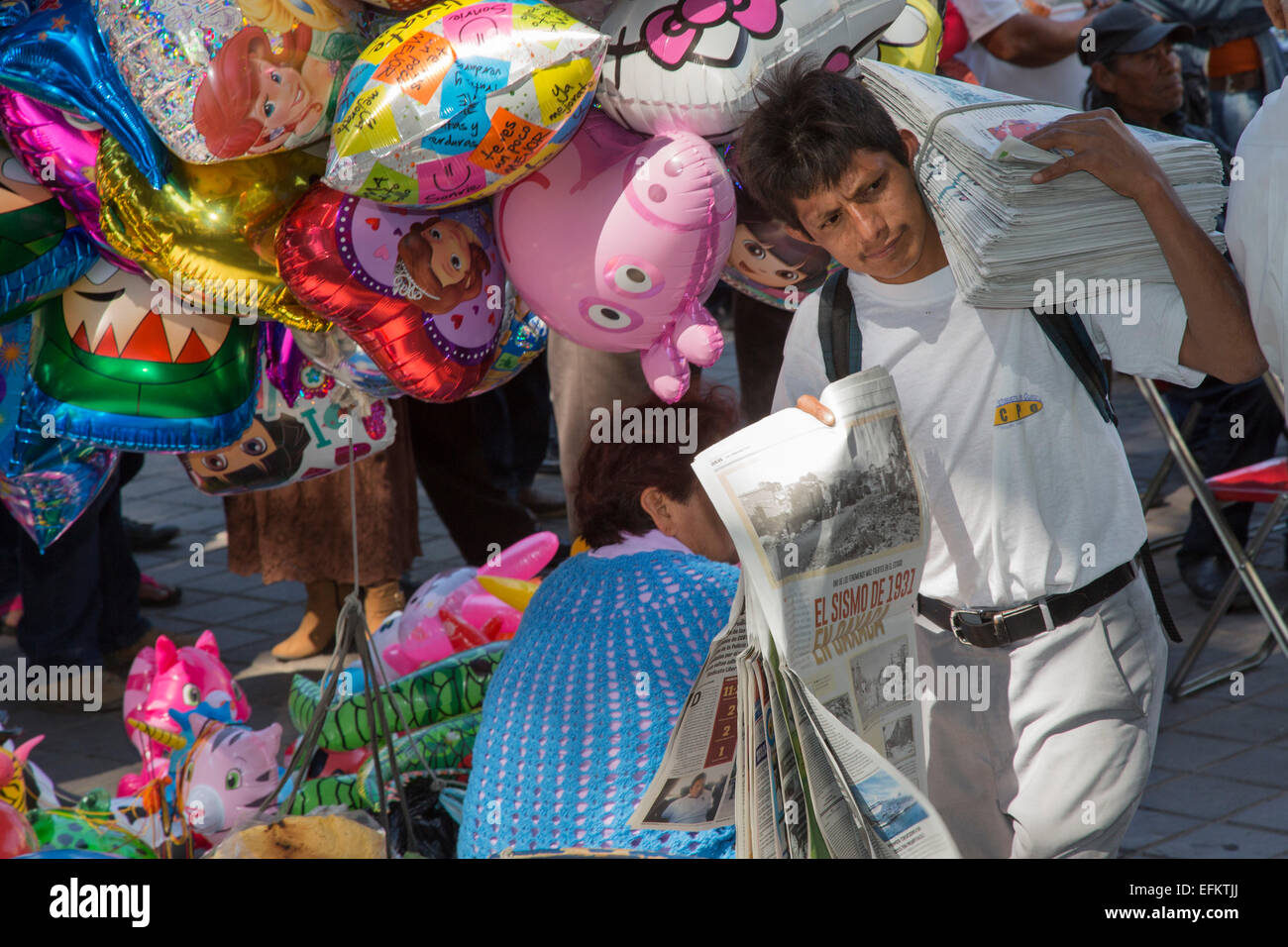 Oaxaca, Mexico - A man selling newspapers in the zócalo (central square) walks past a woman selling balloons. Stock Photo