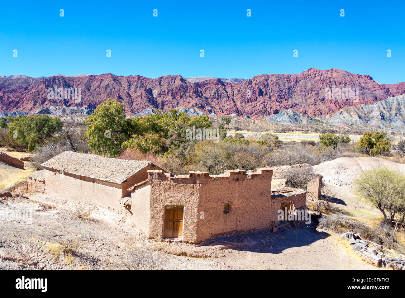 Rustic old building made of adobe with dramatic red hills rising in the background in the small town of Chacopampa near Tupiza, Stock Photo