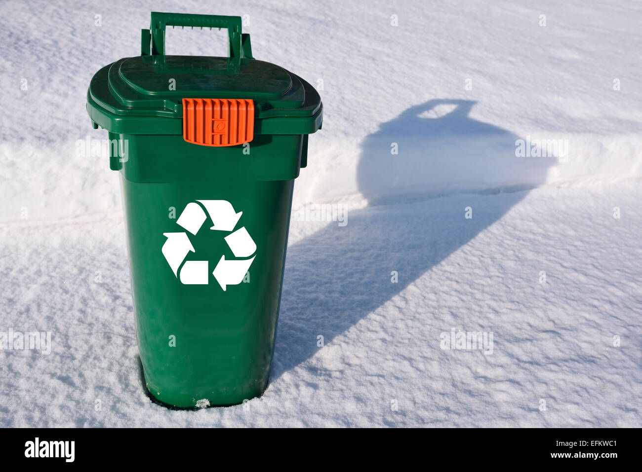Green recycling bin with white logo on snow covered sidewalk waiting for street pickup Stock Photo