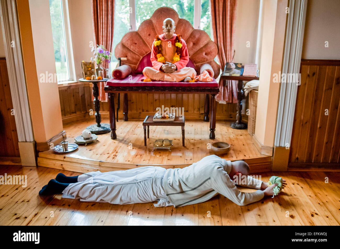 A Hare Krishna devotee wearing white robes prostrates himself in front of a statue of A.C. Bhaktivedanta Swami Prabhupada founder of the Hare Krishna Movement. Stock Photo