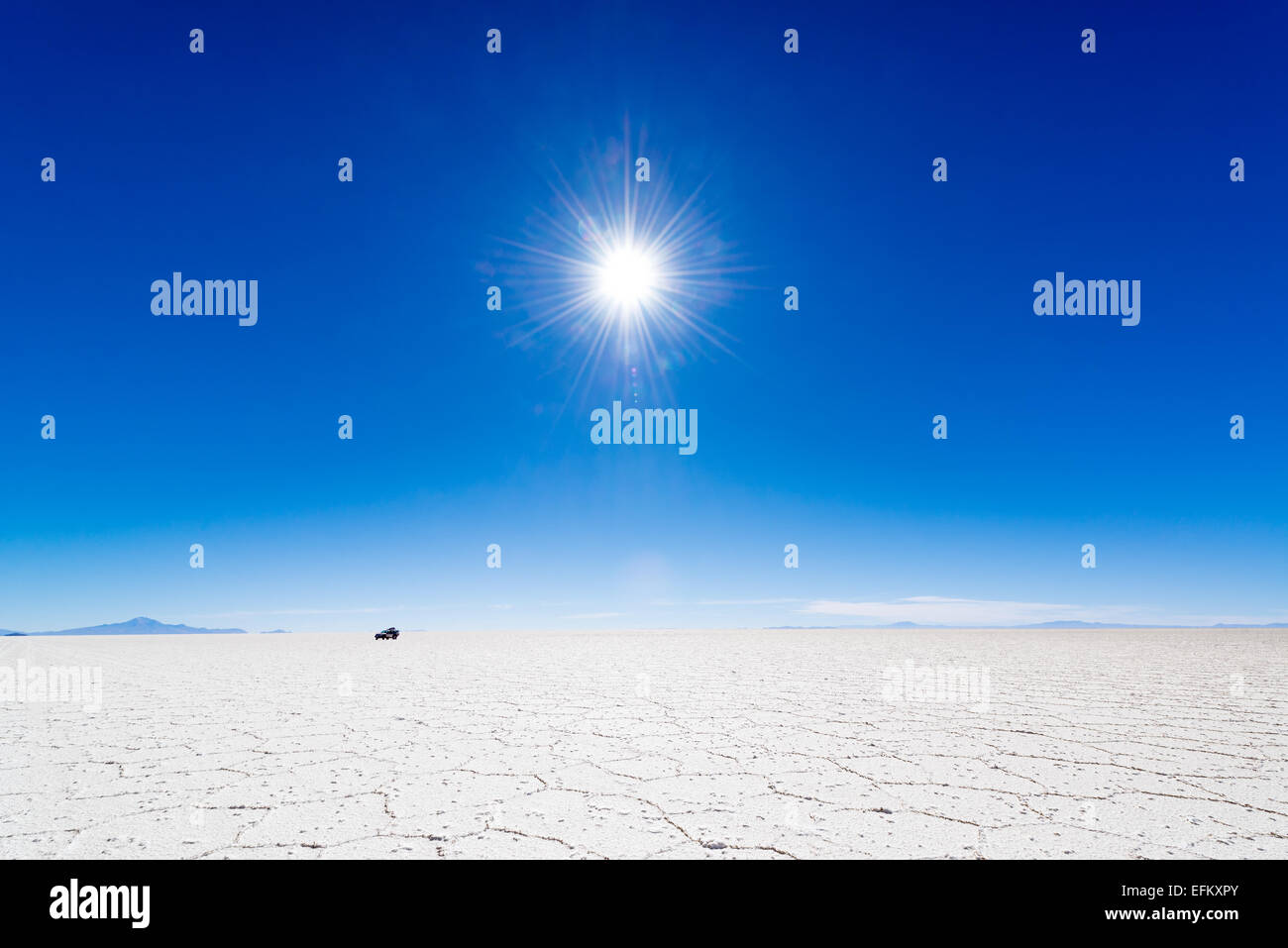 View of the sun over the Uyuni Salt Flats in Bolivia with an SUV in the background. Stock Photo