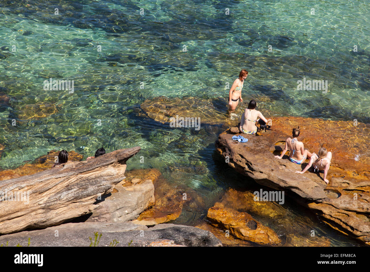 women sitting on a rock in Gordon's Bay, Sydney, Australia Stock Photo