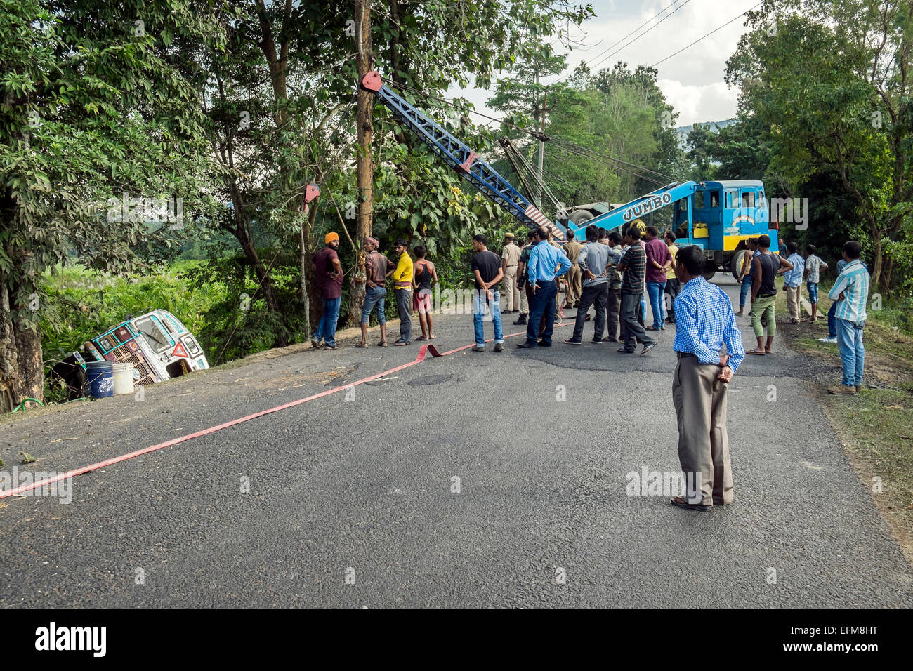 A traffic road accident in Assam North East India where a lorry has come off the road and a mobile crane is trying to rescue it Stock Photo