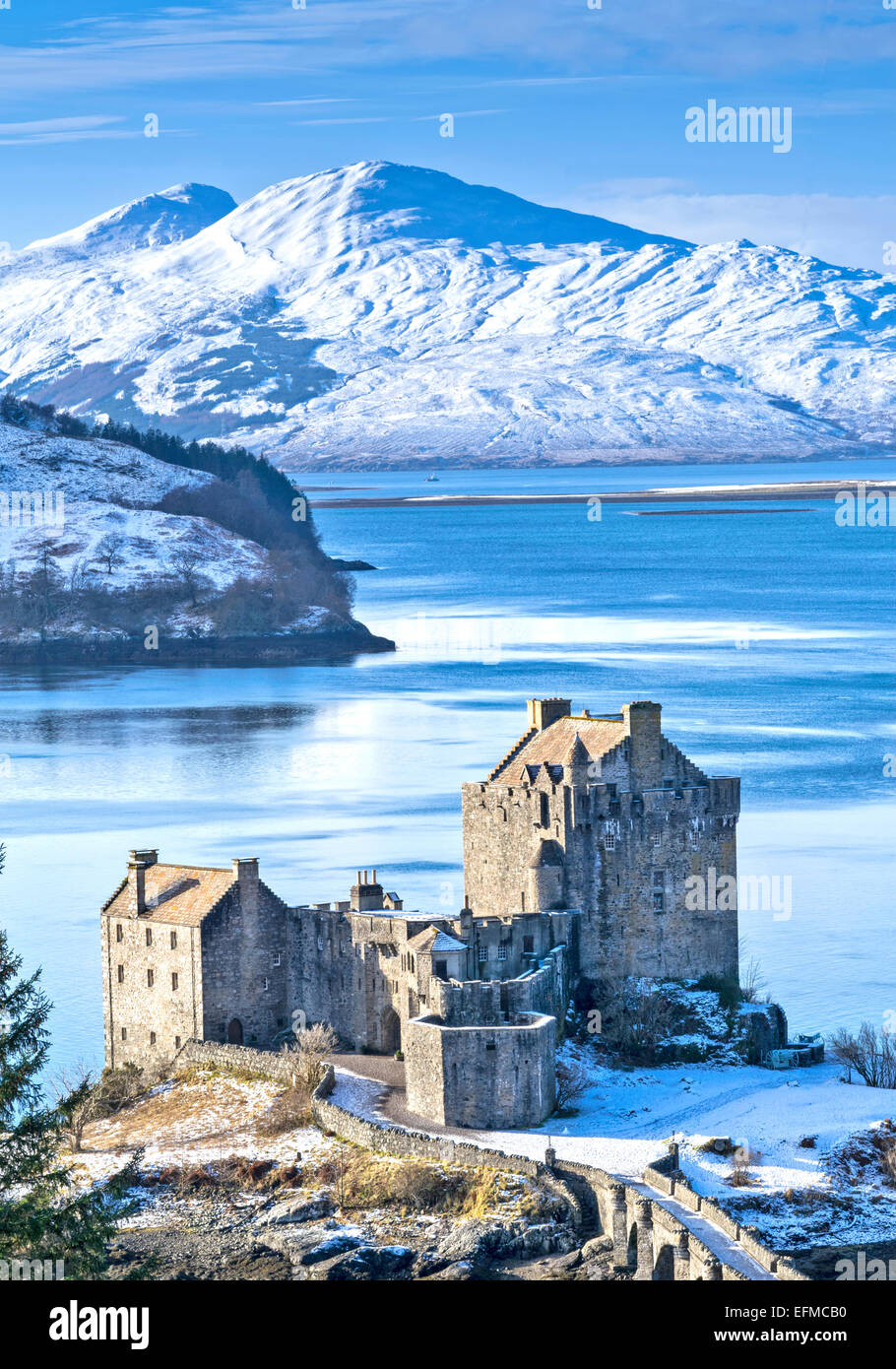EILEAN DONAN CASTLE IN WNTER WITH A BLUE LOCH DUICH AND HEAVY SNOW ON THE MOUNTAINS Stock Photo
