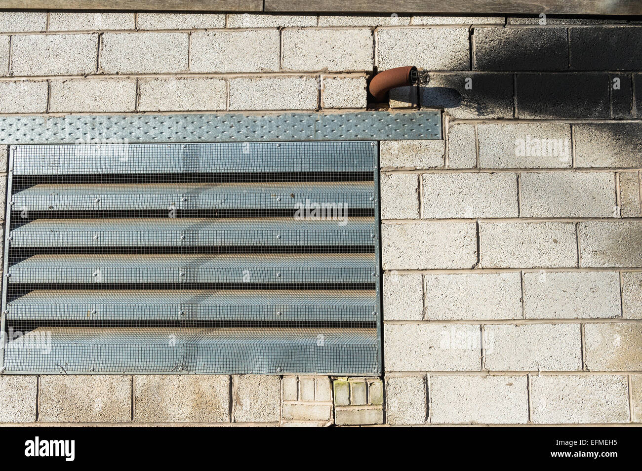 Metal exhaust pipe coming from a block built building with soot stains. Stock Photo
