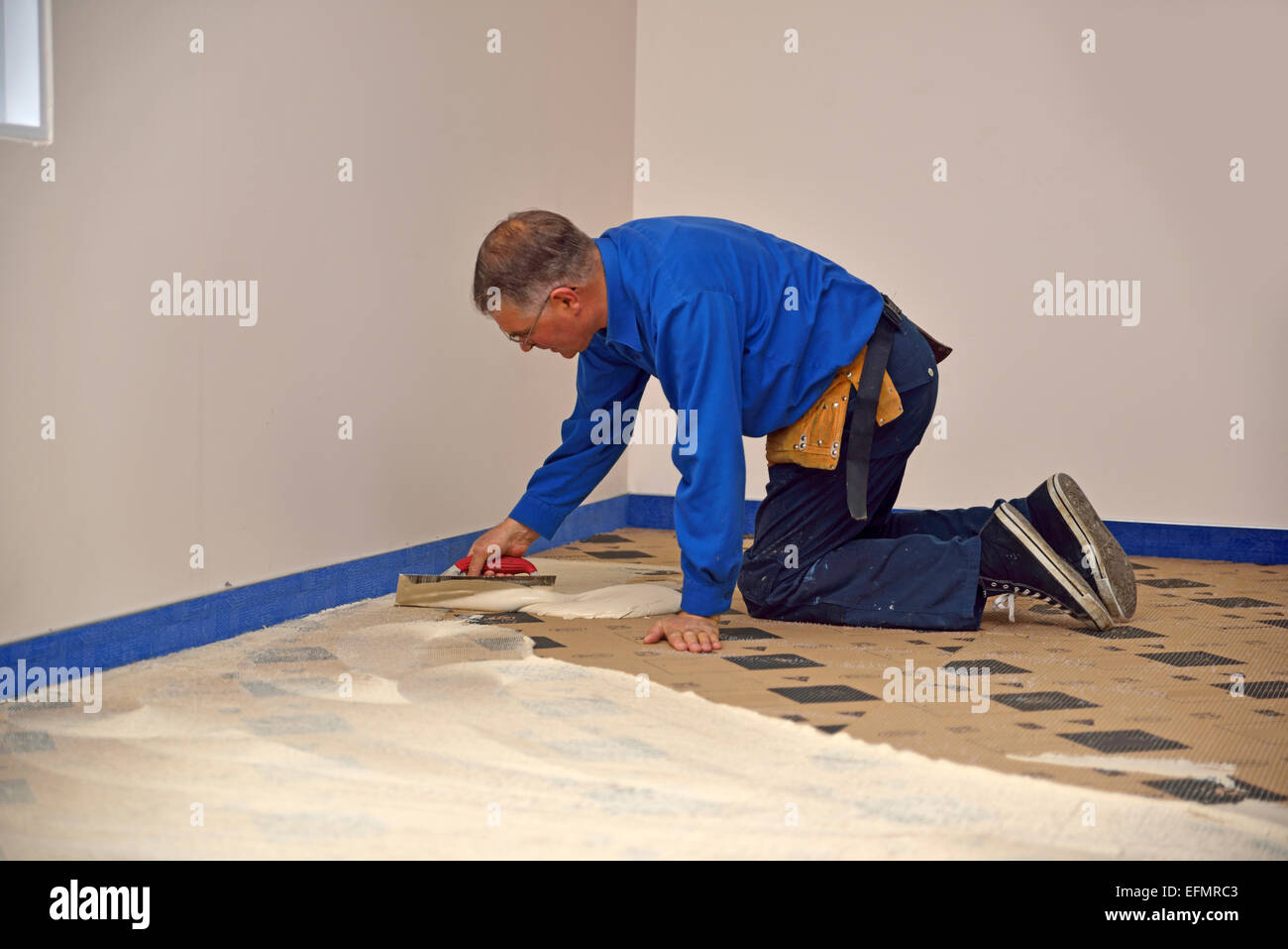 A floorlayer spreads adhesive on the underlay for a carpet laying job