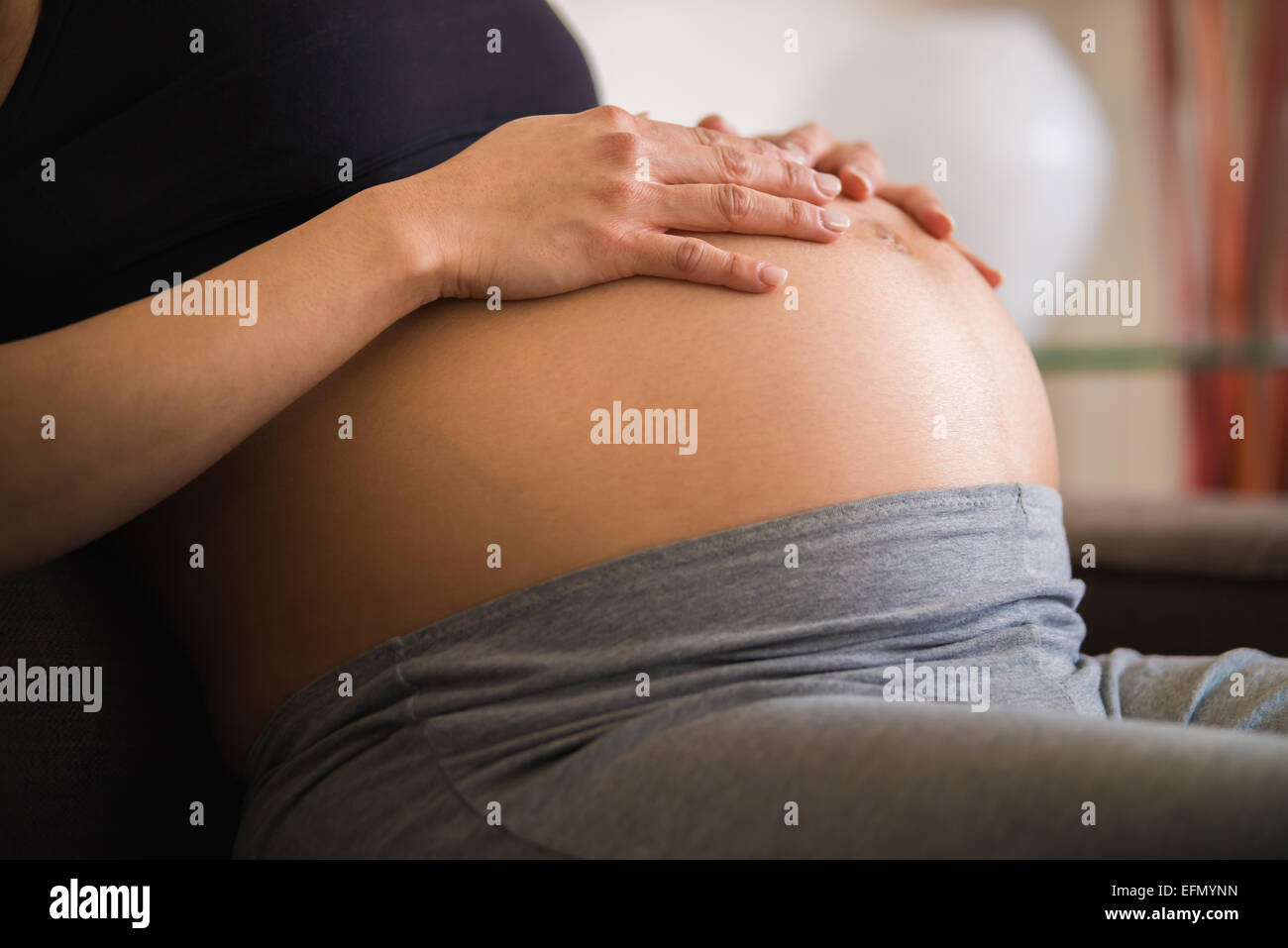 Baby bump, Image of an 8 month pregnant woman sitting on a couch, resting her hands on her baby bump belly. Stock Photo