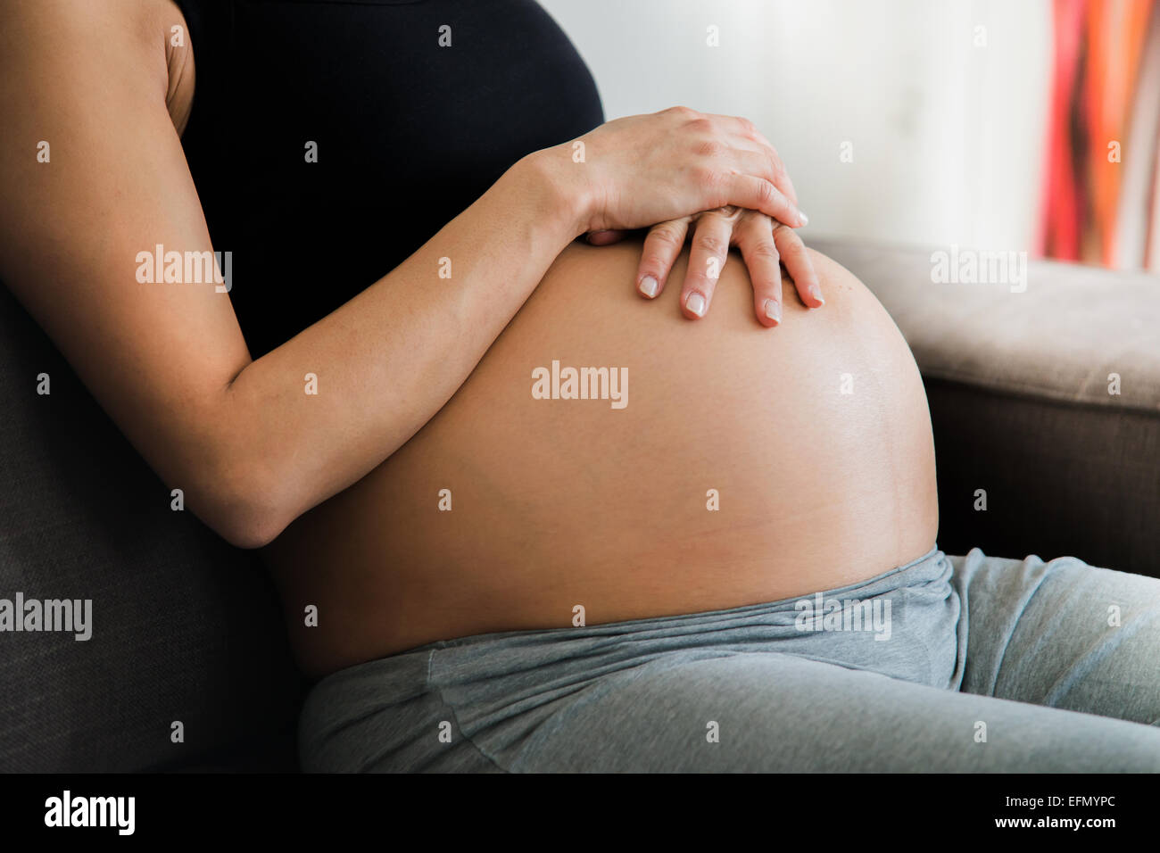 Baby bump, Image of 8 month pregnant woman sitting on a couch holding her bump belly Stock Photo