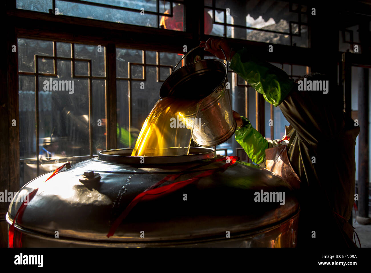 traditional brewing technique of Chinese rice wine: worker pouring the newly produced rice wine to a big pot for storage. Stock Photo