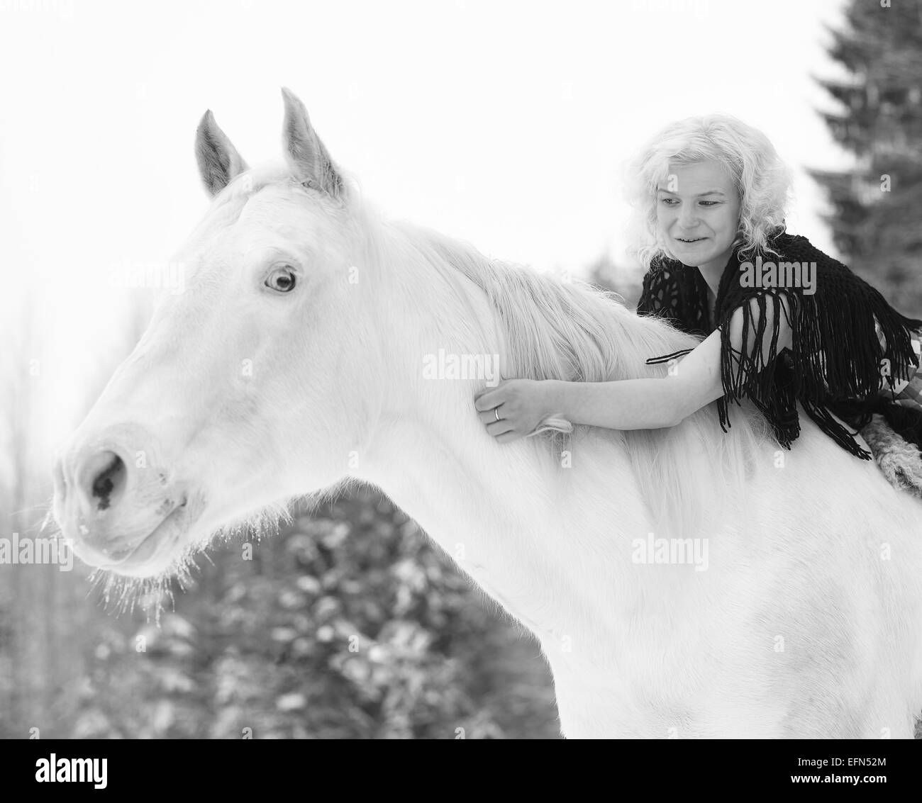 Attractive blond woman hugs a white horse, overcast winter day Stock Photo