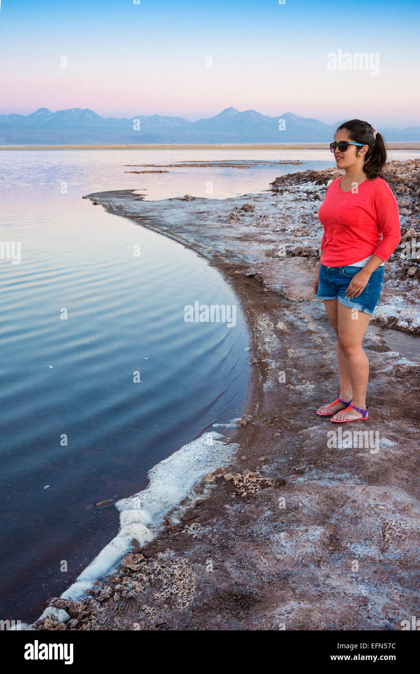 Woman stands on edge of salt-encrusted shore of Tebenquiche lagoon at sunset, San Pedro de Atacama desert, Chile, South America Stock Photo