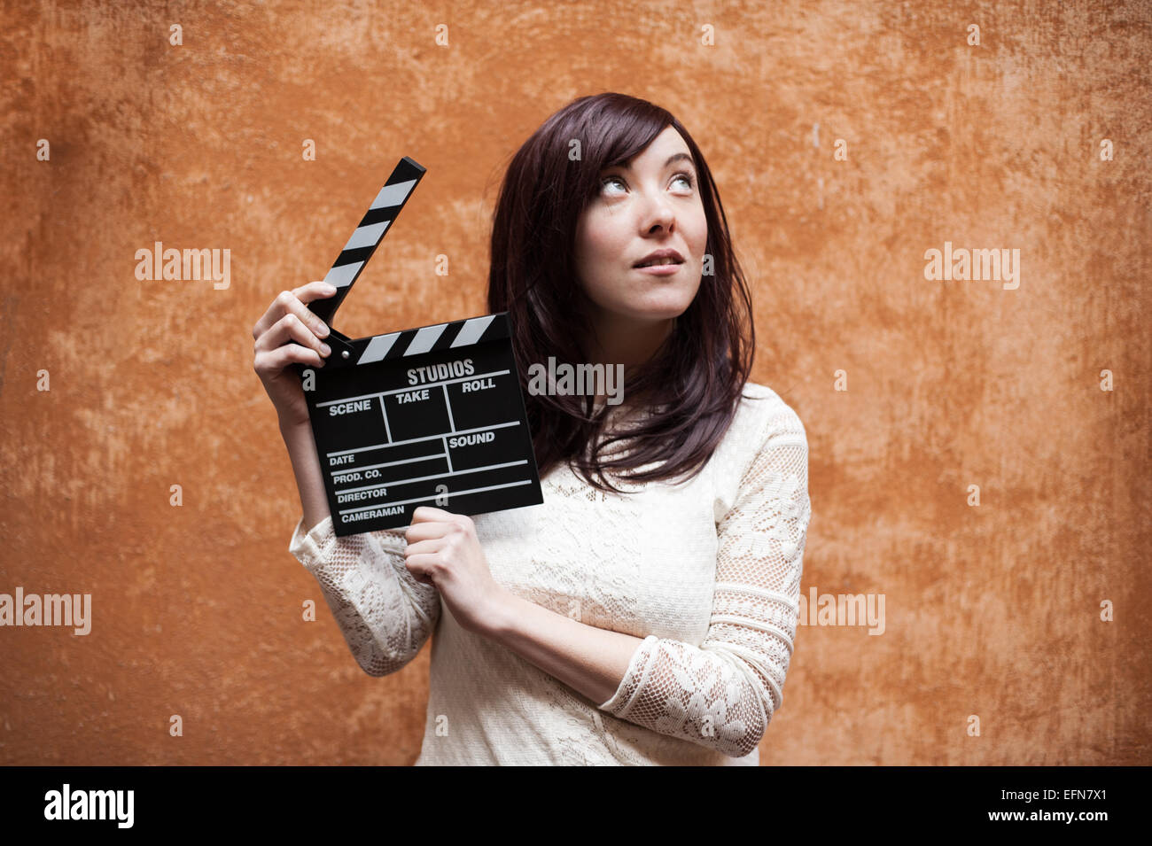 Young woman in 70s hippie style closeup with clapperboard, outdoor orange wall background Stock Photo